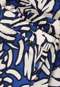 Gros plan sur un tissu avec un motif floral abstrait bleu, blanc et noir et un détail de taille élastique froncée.