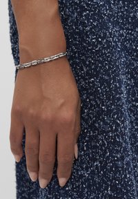 Primo piano di una mano che indossa un bracciale in argento su uno sfondo di tessuto blu scuro e textured.