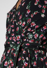 Blommig omlottklänning med svart bas, röda och rosa blommor, gröna inslag och ett strukturerat, flödande tyg.