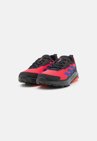 Rote und schwarze Sportschuhe mit blauen Akzenten, oberes Material aus strukturiertem Stoff, Gummilaufsohle und kontrastierenden orangen Details.