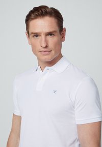 White polo shirt made of cotton with a two-button placket and a small embroidered logo. Short sleeves and a straight fit design.