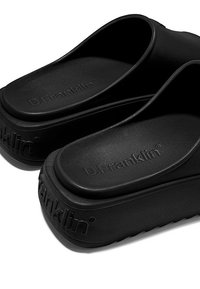 Sandalias de plataforma negras con textura de goma suave y suela elevada. Presentan una marca grabada y un diseño simple y minimalista.