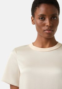 Roomkleurig T-shirt met een ronde hals, korte mouwen en een gladde textuur. Minimalistisch ontwerp met subtiele stikseldetails.