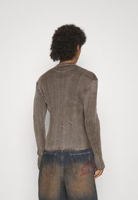 Ribbed brown sweater with a high neckline and fitted silhouette, paired with blue denim jeans featuring a red star embroidery on the back pocket.