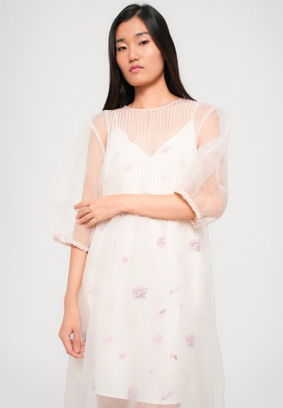 Virágmintás, áttetsző világos rózsaszín ruha csíkos dekoltázzsal és puffos ujjakkal, finom részletekkel a mandzsetták és az alj körül.