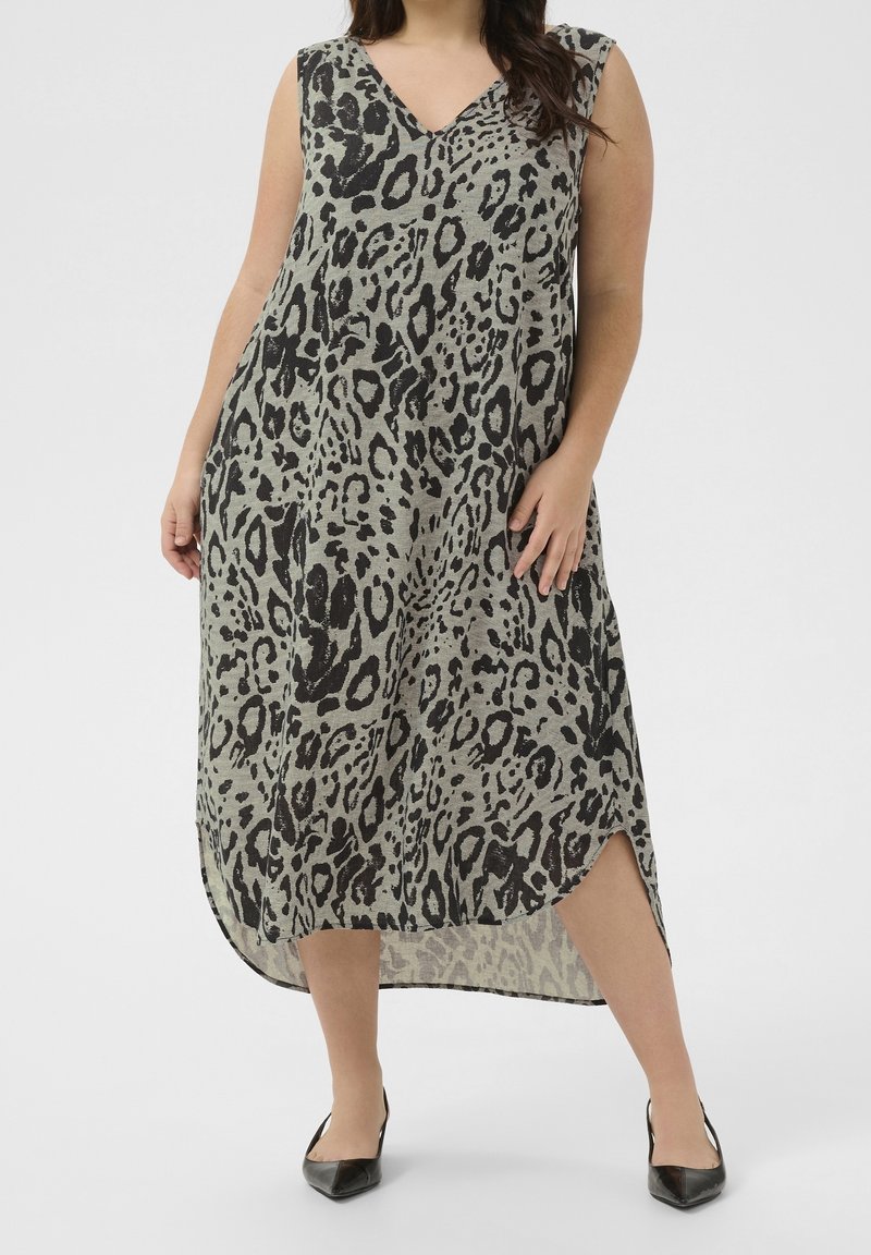 Femme portant une robe sans manches, en V, longue jusqu'aux chevilles, à imprimé léopard, avec un ourlet incurvé et des fentes sur les côtés, associée à des ballerines noires pointues.