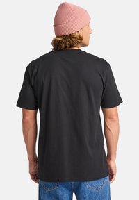 Sort bomulds t-shirt med klassisk pasform, korte ærmer og rund halsudskæring, båret med blå denim jeans og en lys pink ribbet hue.