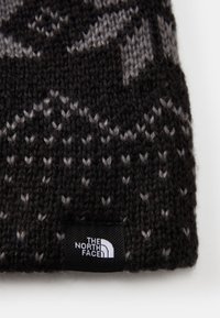Μαύρο και γκρι πλεκτό σκουφάκι με υφασμάτινο σχέδιο, που διαθέτει μικρή λευκή ετικέτα με το λογότυπο "THE NORTH FACE".