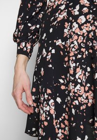 Svart klänning med ett blommönster i rosa och vitt, med långa, puffiga ärmar, mjuk textur och en knapprad framtill.