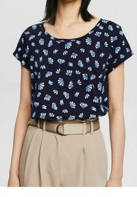 Granatowy t-shirt z krótkim rękawem w kwiatowy wzór w jasnoniebieskim kolorze. Miękka tkanina, okrągły dekolt, luźny krój, w zestawie z beżowymi spodniami z wysokim stanem i paskiem.