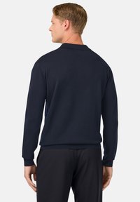 Temno modra pulover s dolgimi rokavi in rebrastimi manšetami. Mehak pleten material s preprostim dizajnom, ki ima klasičen ovratnik.