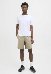 Un tricou alb cu mânecă scurtă, pantaloni scurți bej, încălțăminte sport neagră, șosete albe. Design simplu, croială normală, fără modele sau logo-uri vizibile.