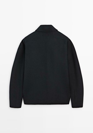 Veste noire à col vue de dos, présentant un design structuré, une texture lisse et des lignes épurées sans matériel ni embellissements visibles.
