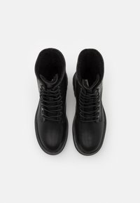Botas de cuero negras hasta el tobillo con diseño de cordones, puntera redonda y forro interior suave; suela de goma plana con ligera textura.