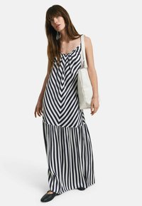 Maxikleid mit gestreiftem Design in Marineblau und Weiß, mit gerafftem Ausschnitt und ausgestelltem Saum. Kombiniert mit einer beige Tasche.
