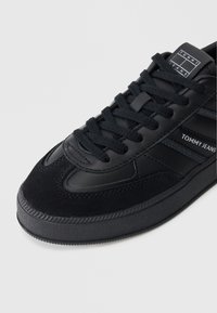 Fekete sneaker sima bőr felsőrésszel, velúr részletekkel, texturált gumitalppal és három csíkkal, valamint logóval az oldalon.