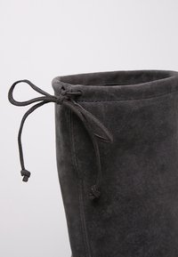 Botte en daim noir avec un dessus rond, dotée d'une fermeture à cordon pour un ajustement réglable. Texture douce avec une finition lisse et des coutures renforcées.