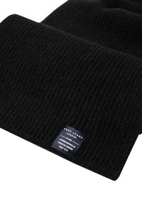 Melnas ribotas adītās šalles ar tumši zilu etiķeti, uz kuras rakstīts "Pepe Jeans London, Denim brand Co, Since 1973", vienā galā.