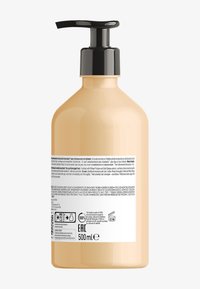 Brun plastpumpflaska med svart pumpkork. Etiketten visar produktinformation på flera språk och symboler på baksidan. Kapacitet: 500 ml.