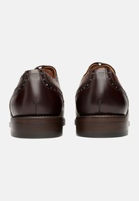 Dunkelbraune Leder Schuhe mit Brogue-Details, abgerundetem Zeh und einem gestapelten Holzabsatz, mit einer glatten Oberfläche und subtilen Nähten.