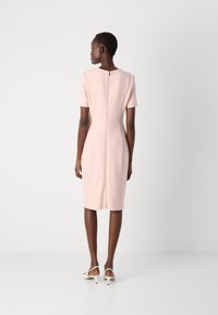 Fitted, short-sleeve dress in light pink fabric. Back zip closure, knee-length hem, smooth texture. Worn with beige high-heel shoes.