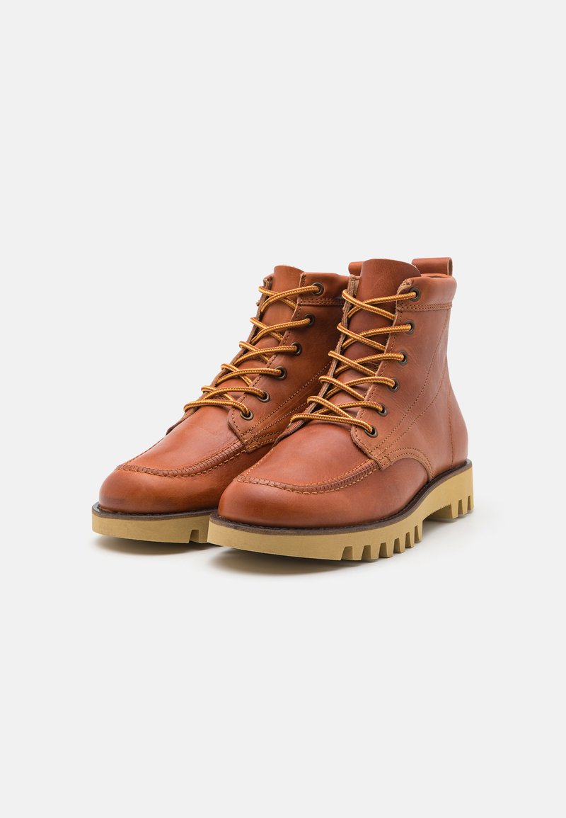 Botas de cuero marrón hasta el tobillo con cordones amarillos, puntera redonda, detalles cosidos y suela de goma con relieve. Textura suave y diseño de altura media.