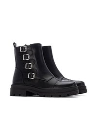 Botas de tobillo de cuero negro con tres hebillas plateadas, punta redondeada, parte superior texturizada y suela de goma gruesa. Cuenta con una pestaña para facilitar su uso.