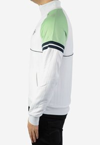 Chaqueta deportiva blanca con un cuello alto, detalles en verde en los hombros, franjas negras en las mangas y puños acanalados, con un acabado texturizado.