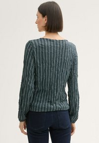 Langarmbluse in Dunkeltürkis mit einem strukturierten Wellenmuster und einem Rundhalsauschnitt. Verfügt über geraffte Ärmel und eine taillierte Silhouette.