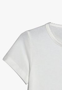 Bijela pamučna majica s okruglim izrezom i kratkim rukavima. Meki, glatki materijal s ušivenim šavovima i dekorativnim rubom na izrezom vrata.