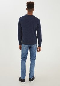 Felpa marina con un motivo testurizzato di felce, abbinata a jeans azzurri chiari. Le calzature presentano suole nere con accenti bianchi.
