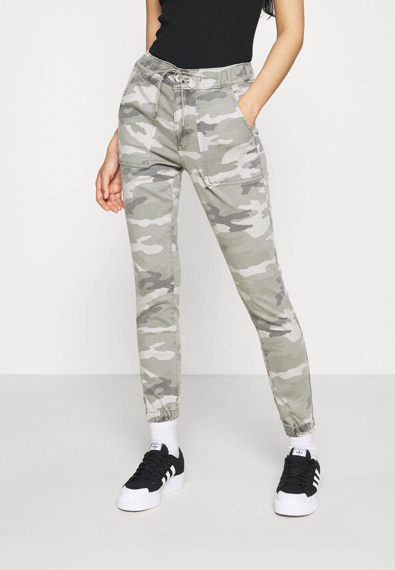 Kamouflage joggerbyxor i grå och gröna nyanser, med elastisk midja, sidofickor och avsmalnande muddar, kombinerade med svarta sneakers.