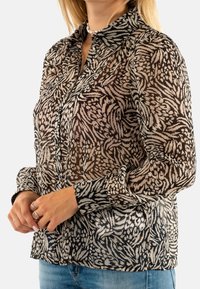 Blusa trasparente con un motivo floreale nero e beige. Presenta un colletto, chiusure con bottoni e maniche lunghe con estremità a polsino.
