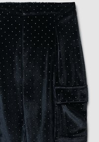 Pantaloni di velluto nero con una texture morbida, impreziositi da piccoli strass bianchi e un dettaglio di risvolto su un lato.