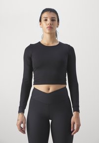 Zwarte cropped top met lange mouwen, gemaakt van een gladde, rekbare stof, gecombineerd met zwarte high-waisted leggings met een kruislings ontwerp voor de tailleband.