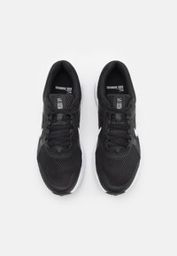 Baskets de course noires avec une tige en mesh, présentant un logo swoosh blanc, des lacets plats et une semelle texturée, conçues pour la respirabilité et le confort.