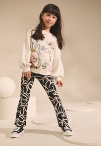 White sweatshirt with puffed sleeves, featuring floral and text designs. Black flared pants with a cream abstract leaf pattern. Black shoes.