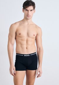 Čierne boxerky s logom na páse. Materiál vyzerá hladko a pružne, ponúkajúce priliehavý strih s stredne vysokým pásom.