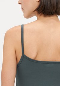 Donkergrijze tanktop met dunne bandjes, met een gladde, zachte textuur en een aansluitend ontwerp, waarbij de achterkant zichtbaar is.