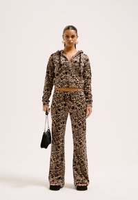 Brun mønstrede to-delte loungewear sæt med en zip-up hættetrøje og flared bukser. Fremstillet af blødt stof, inkluderer snore og lommer.