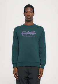 Sweatshirt de algodão verde com um design de logotipo roxo no peito, gola redonda e punhos e bainha canelados. Textura suave, ajuste casual.