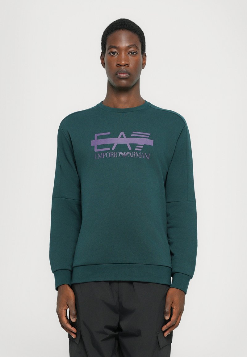 Sweatshirt de algodão verde com um design de logotipo roxo no peito, gola redonda e punhos e bainha canelados. Textura suave, ajuste casual.