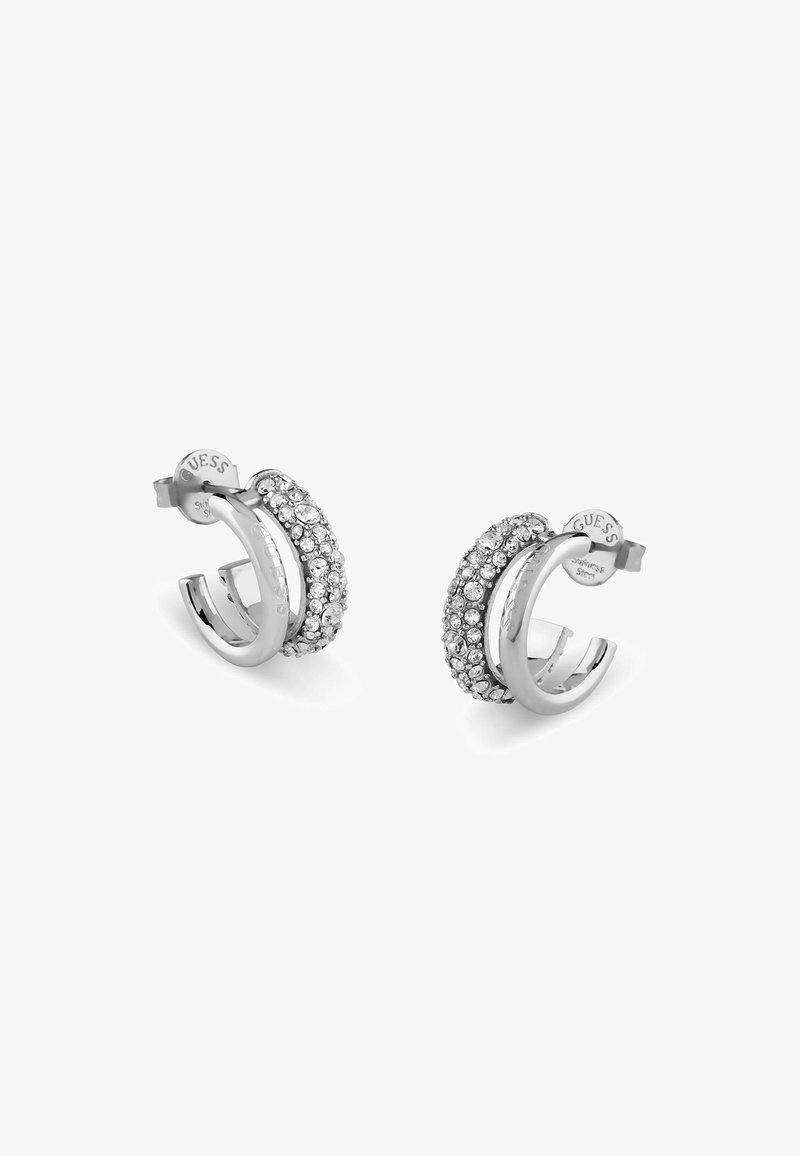 Orecchini a cerchio in argento con un design curvo, decorati con strass trasparenti sulla superficie esterna, dotati di chiusura a gancio e logo del marchio.