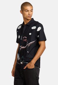 Schwarzkurzes T-Shirt mit einem lebendigen, fotografischen Druck einer Person, mit knöpfbarer Vorderseite und glattem Material.
