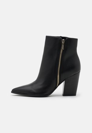 Bottine en cuir noir avec bout pointu, talon bloc superposé et fermeture éclair dorée sur le côté avec tirette logo.