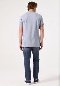 Camiseta de manga corta a rayas en azul claro, mezcla de algodón, corte relajado, combinada con jeans de mezclilla azules y zapatillas oscuras, vista desde atrás.