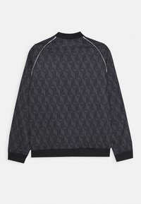 Chaqueta negra con un diseño geométrico. Presenta un cuello, puños y bajo acanalados. Detalle sutil de piping blanco a lo largo de los hombros.