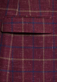 Bordowy materiał w kratkę z niebieskimi i zielonymi liniami. Tekstura jest tkana, co dodaje głębi wzorowi. Zawiera kieszeń naszywaną.