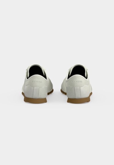 Paire de baskets blanches avec semelles marron vues de dos, comportant le nom de la marque "SANDRO" embossé sur le talon.