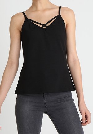 Zwarte mouwloze top met dubbele gekruiste bandjes bij de hals, gedragen met donkergrijze jeans.